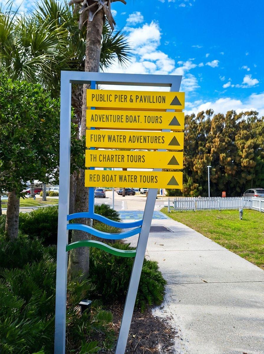 Yellow directional signs at Vilano Beach Pier pointing to Public Pier and Pavilion, Adventure Boat Tours, Fury Water Adventures, TH Charter Tours, and Red Boat Water Tours