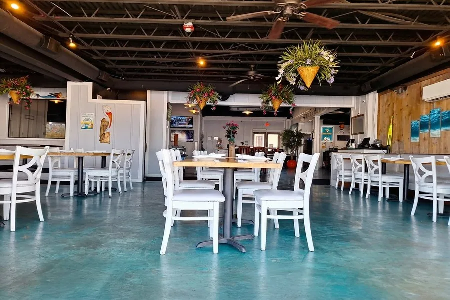Mavi Waterfront Bar & Grill dining room with white chairs, teal concrete floors, and hanging planters